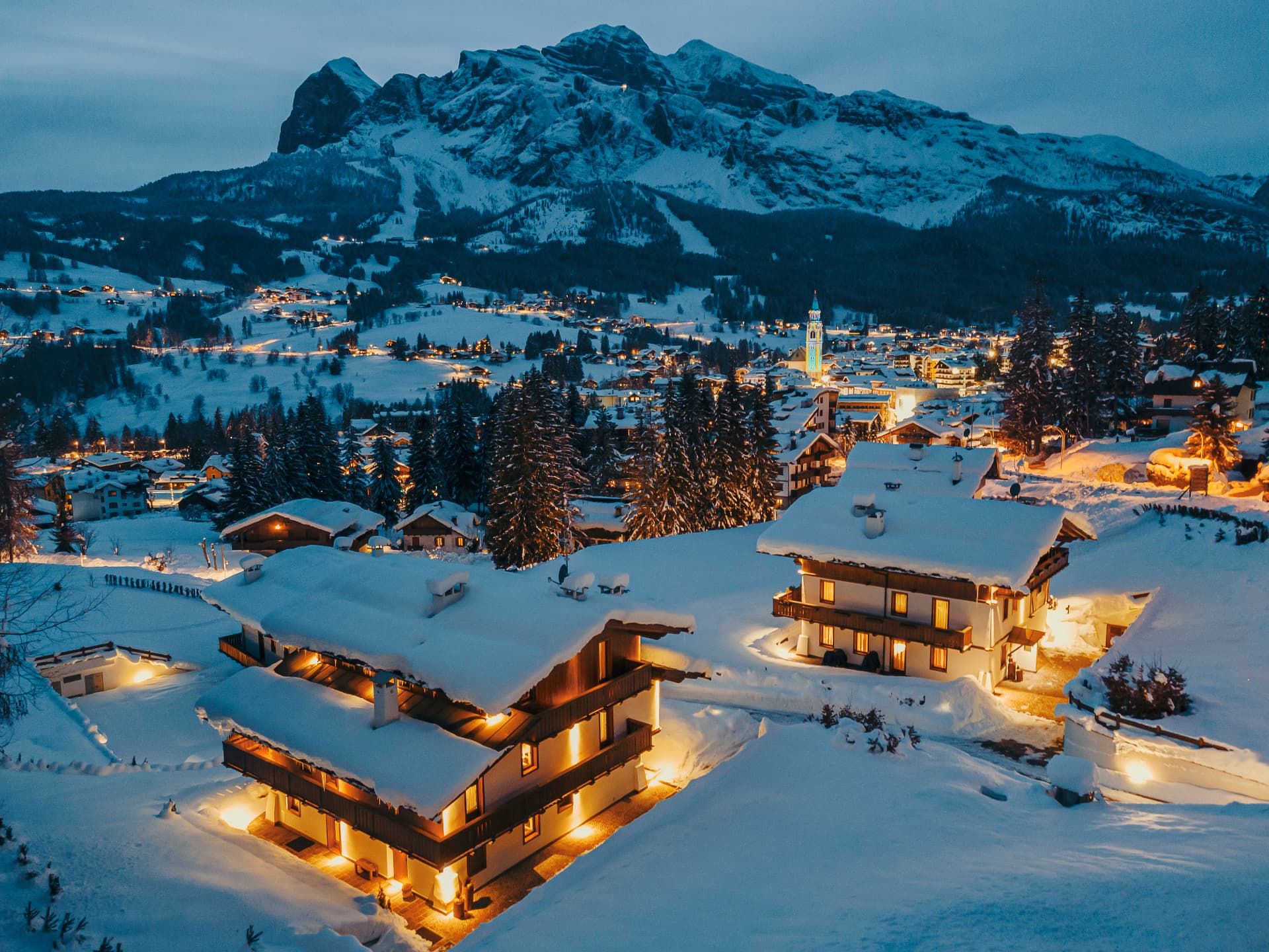 Luxury chalets lit at night above Cortina d'Ampezzo with the snow-covered Dolomite peaks